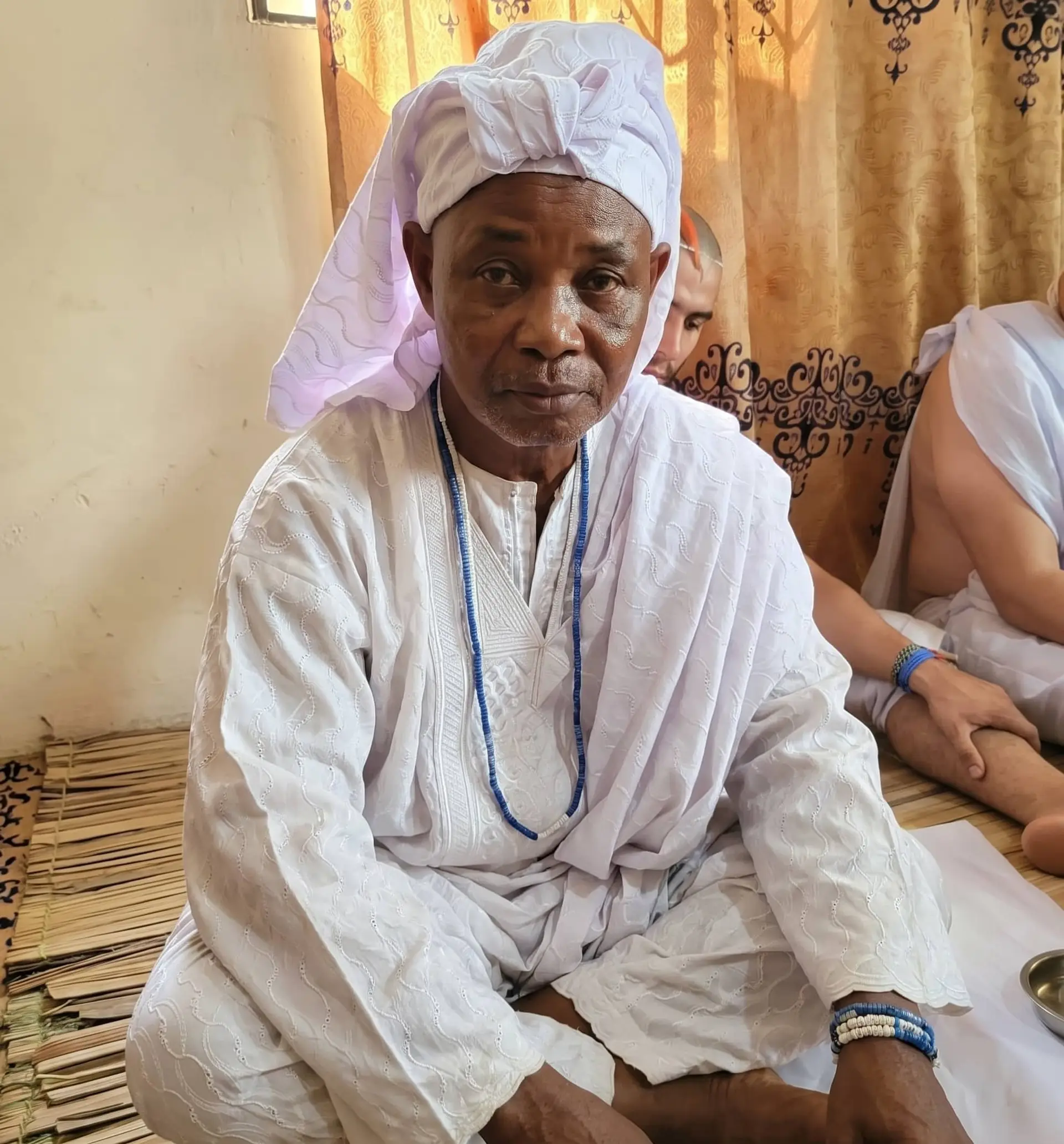 Dr Abdul in white robes and a white turban, seated on a mat with clients during a consultation